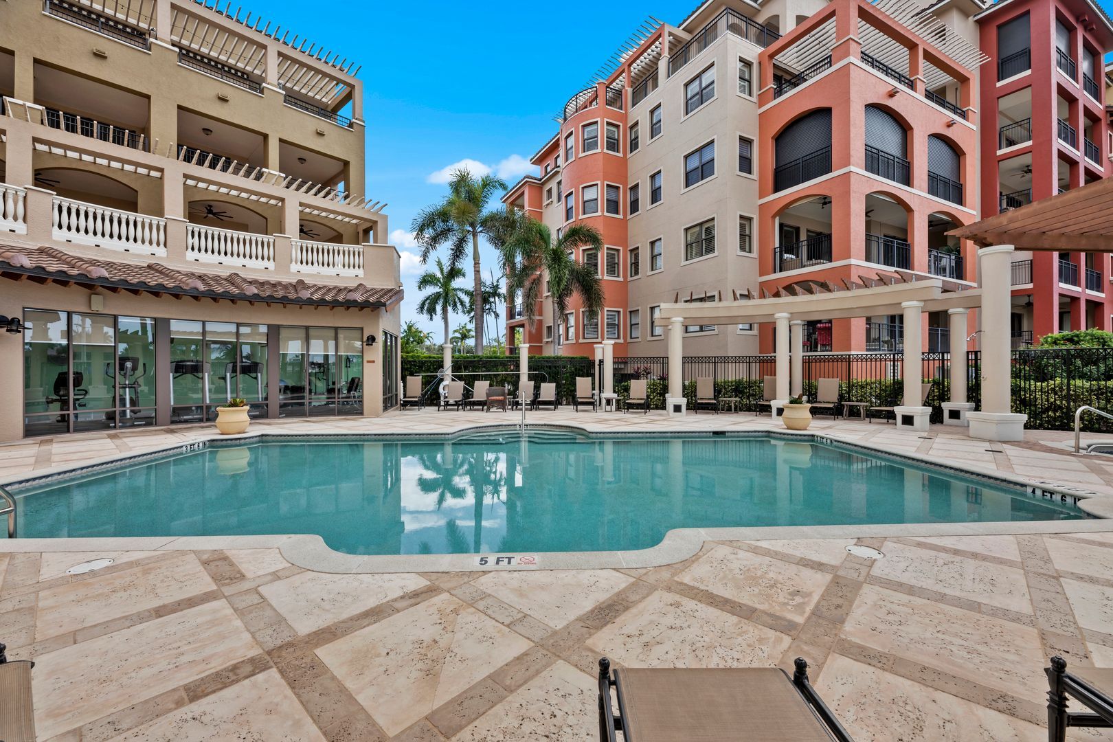 Luxury apartment courtyard with a swimming pool, palm trees, and multi-story buildings under a blue sky
