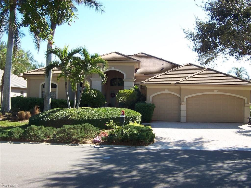Suburban house with a tiled roof, two-car garage, and palm trees along a sunny driveway
