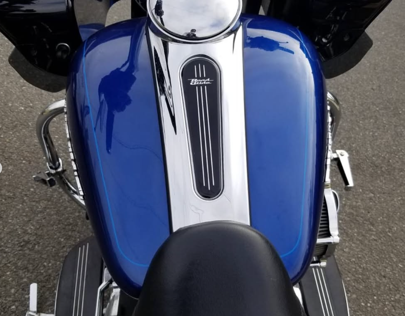 A high-angle view of a bright blue motorcycle gas tank featuring a central chrome console with pinstriping detail.