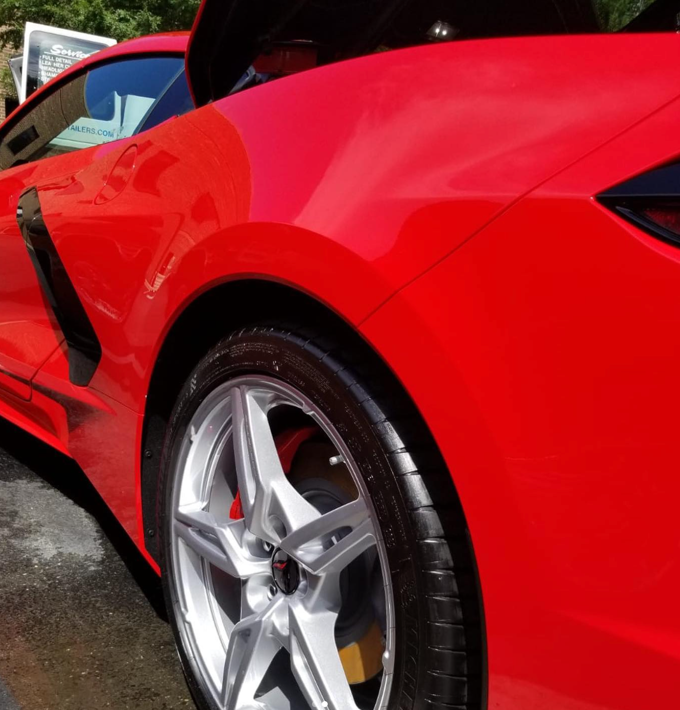A close-up view of the rear side panel and silver five-spoke wheel of a vibrant red sports car.
