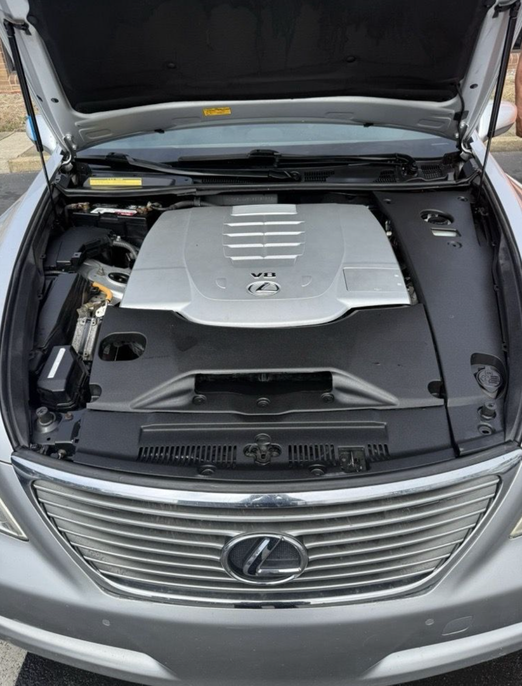 The engine bay of a silver Lexus with its hood open, highlighting the metallic engine cover.