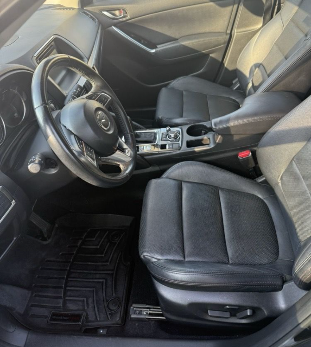The interior of a vehicle featuring black leather bucket seats, a multi-function steering wheel, and rubber floor mats.