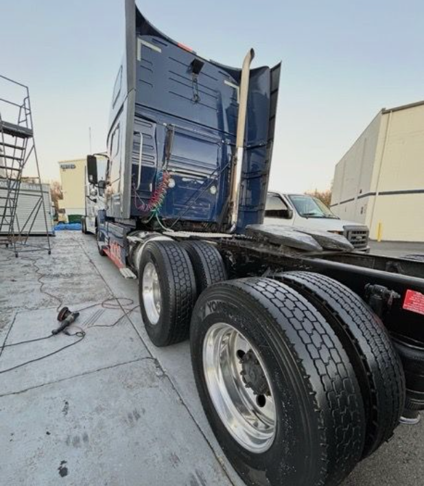 A blue semi-truck parked on a concrete lot, angled to show its rear tires, chassis, and exhaust stack.