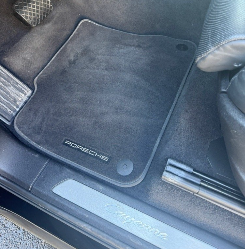 A black Porsche floor mat inside a vehicle with a silver 