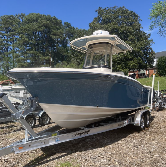 A blue and white center console boat on a trailer parked on a gravel lot under a clear blue sky.