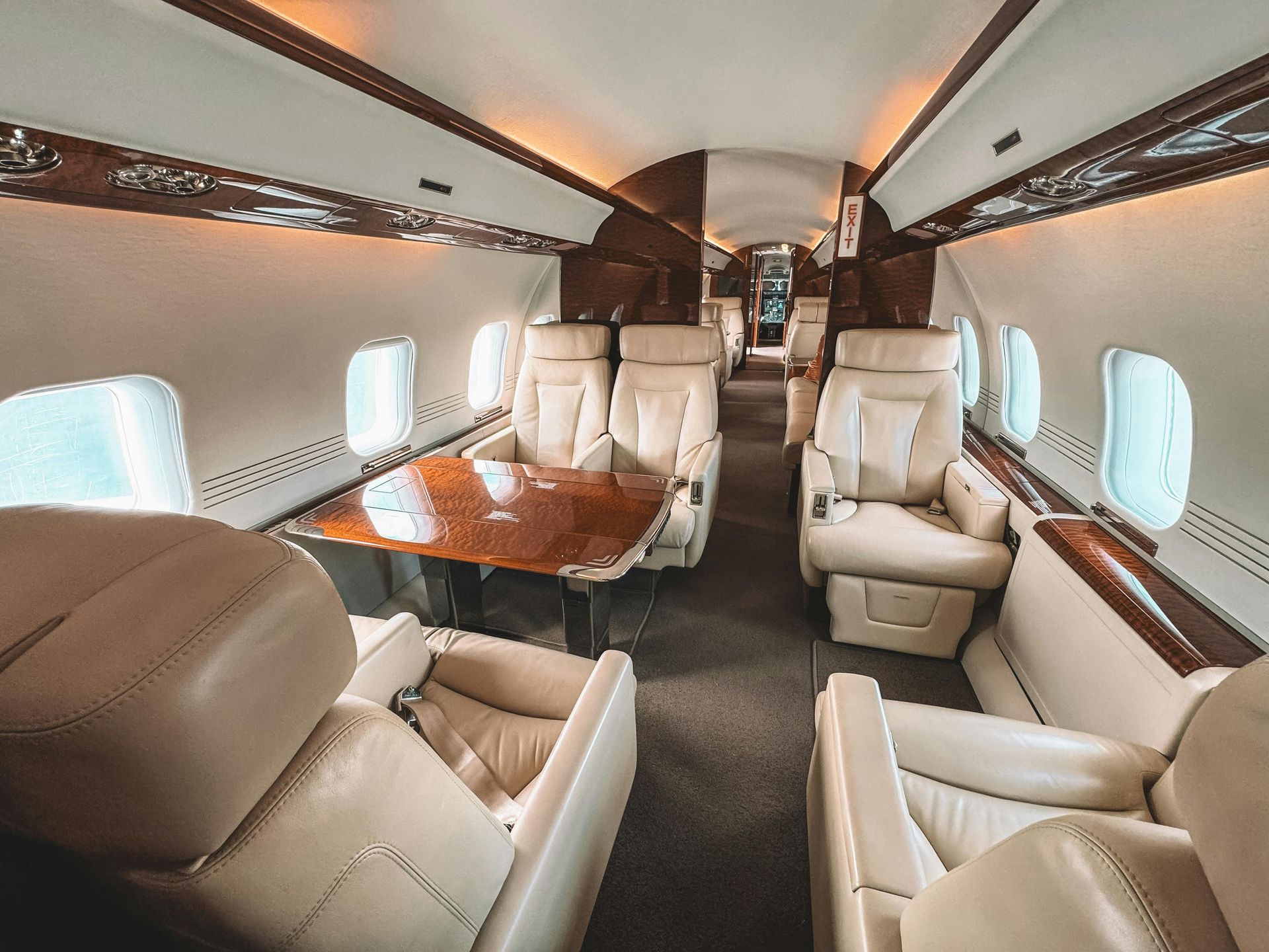 Interior of a private jet cabin featuring cream leather seats, a wood table, and windows arranged in a double club layout.