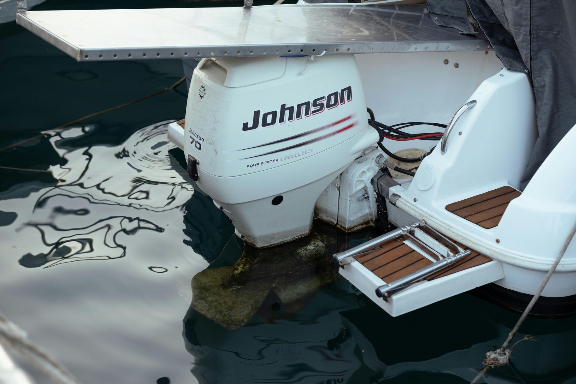 A white Johnson outboard motor mounted on the back of a boat with a swim platform and ladder, partially submerged in water.