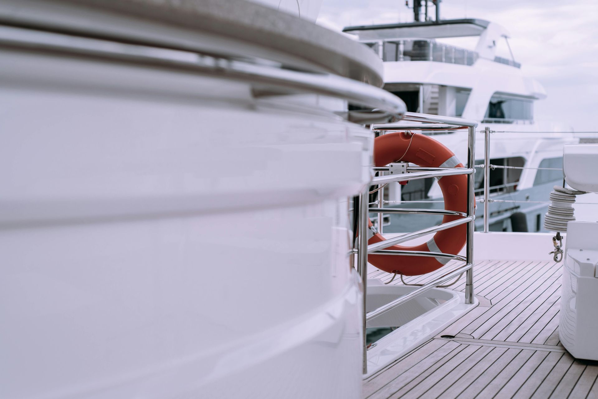 A white yacht deck with a lifebuoy mounted on a railing, with another vessel visible in the background.