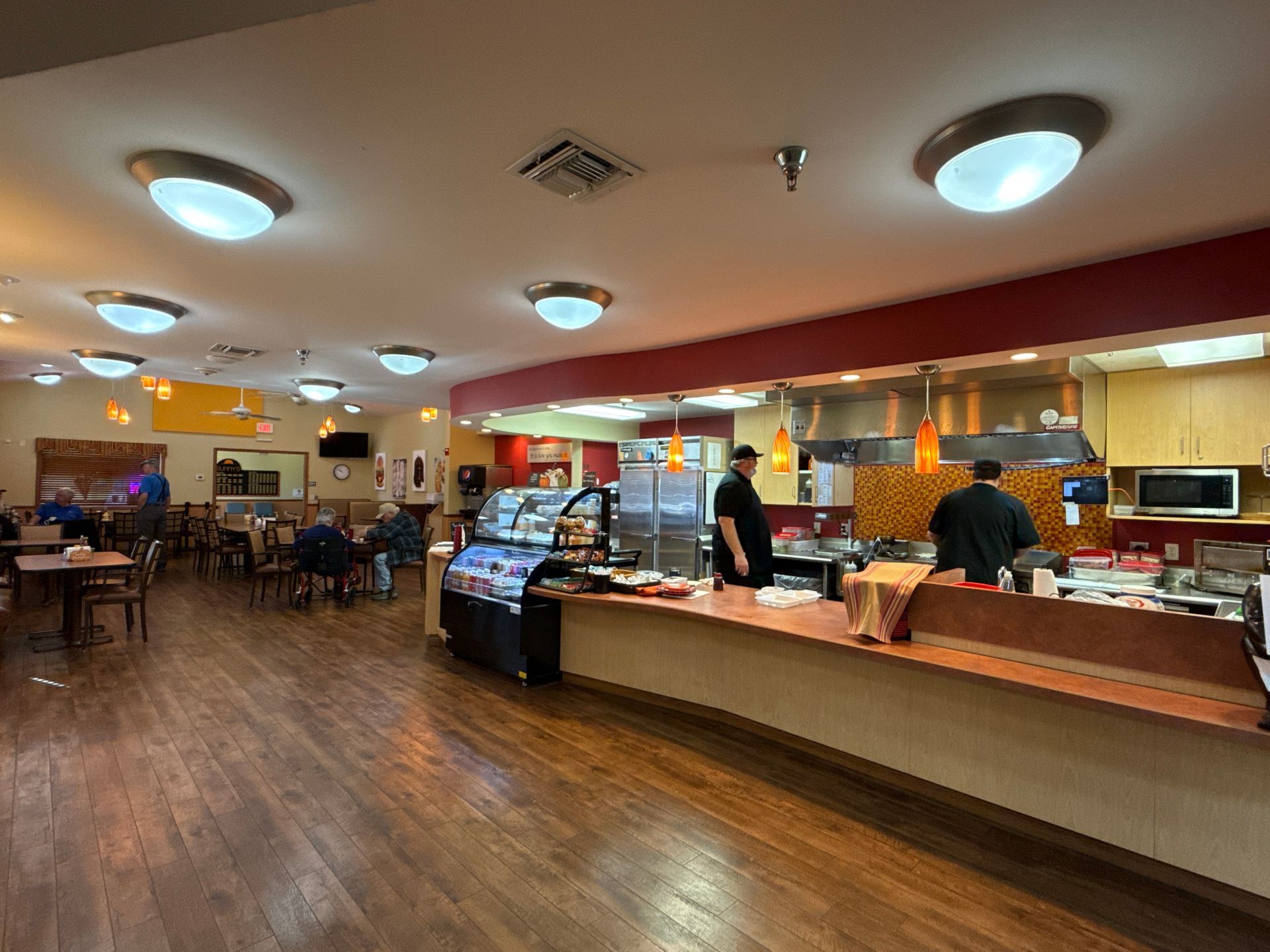 Restaurant interior with counter, kitchen staff, tables, and customers.