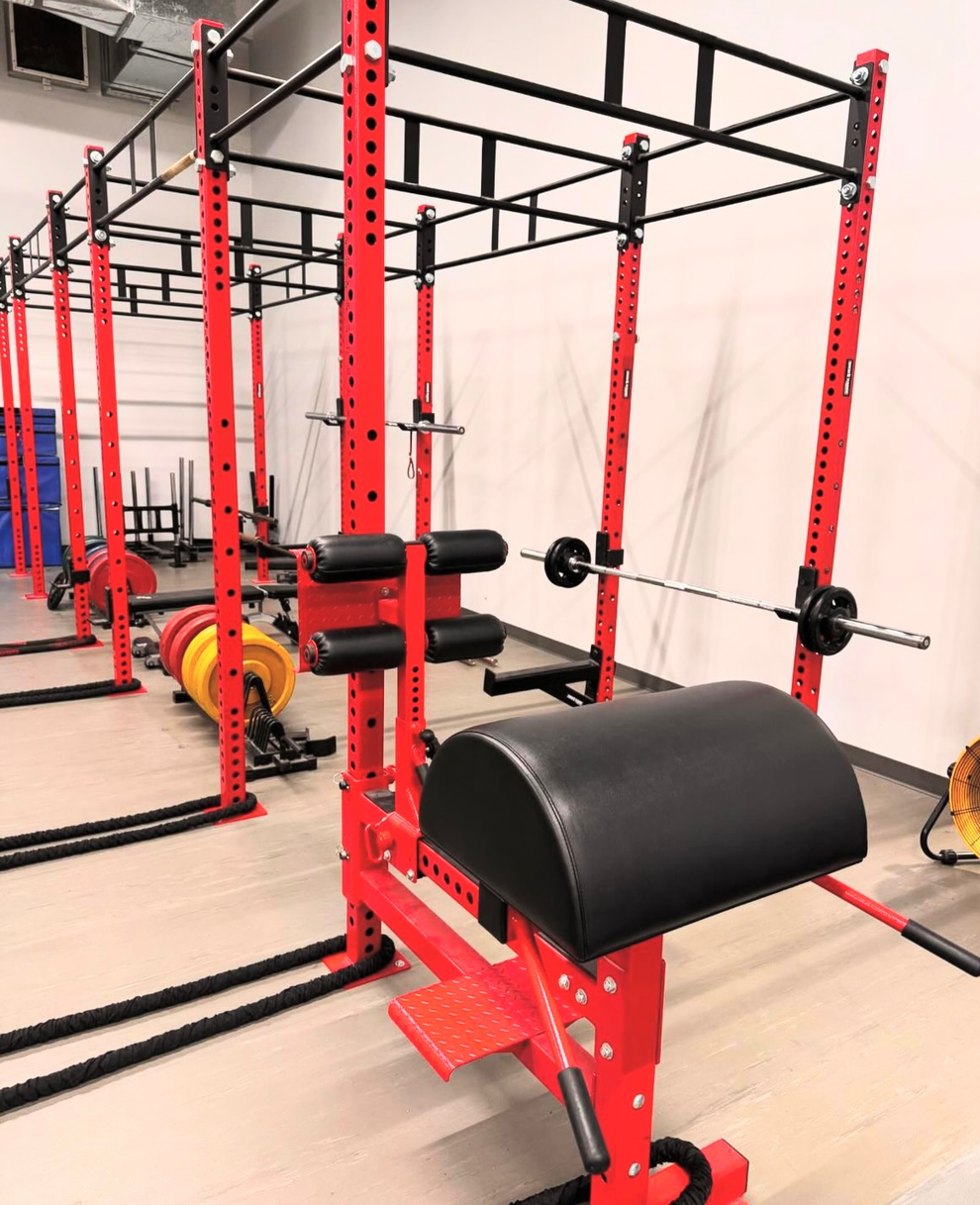Red gym training rack with red and black attachments in a mirrored fitness room in Winnipeg, MB