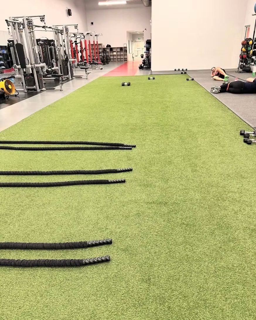 Gym turf lane with battle ropes laid out and weight equipment in the background