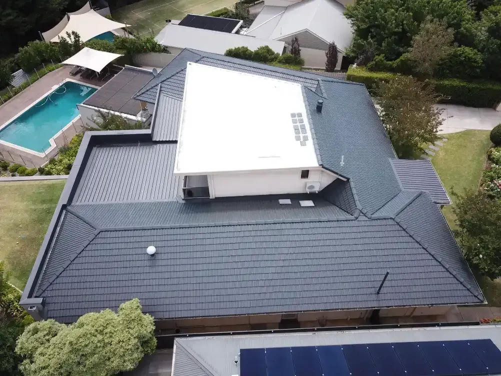 An aerial view of a house with a swimming pool and solar panels on the roof.