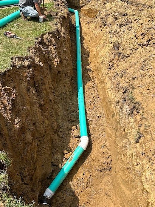 Green drainage pipes installed in a narrow, freshly dug dirt trench outdoors.