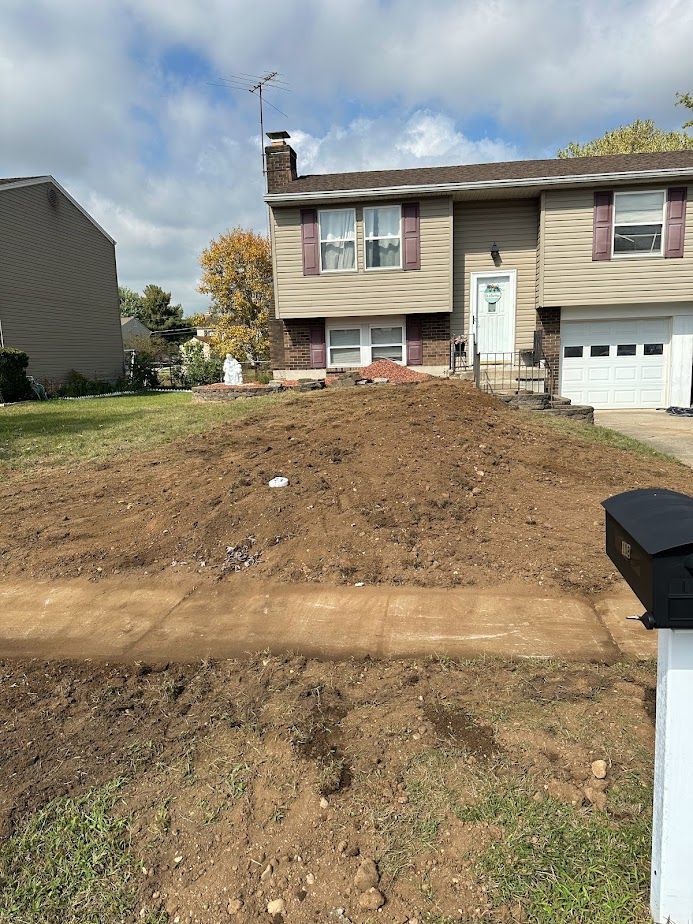 A tan split-level house with a large, freshly disturbed mound of dirt in the front yard near the sidewalk.