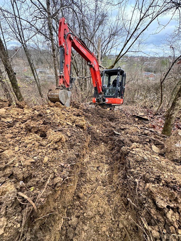 A red excavator parked on a dirt path in a wooded area during winter.