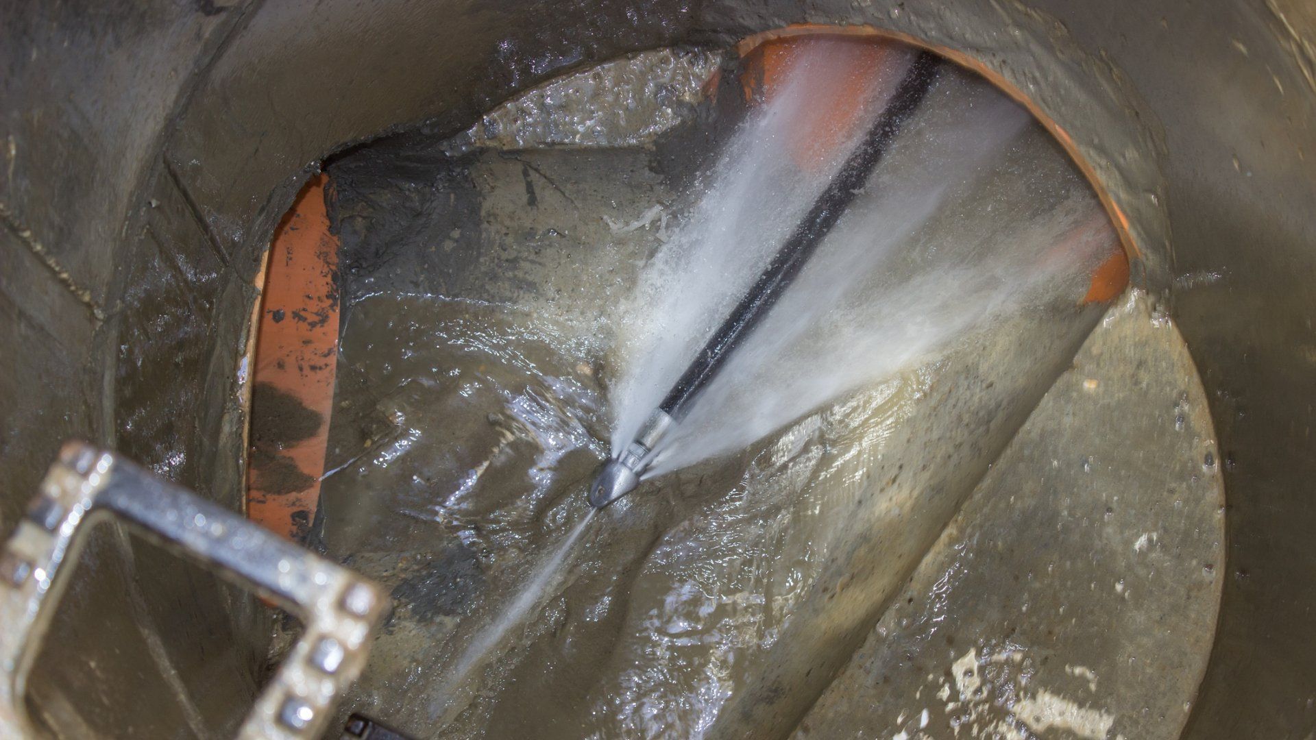 A high-pressure jet hose sprays water into a sewage pipe within a concrete manhole to clear a blockage.