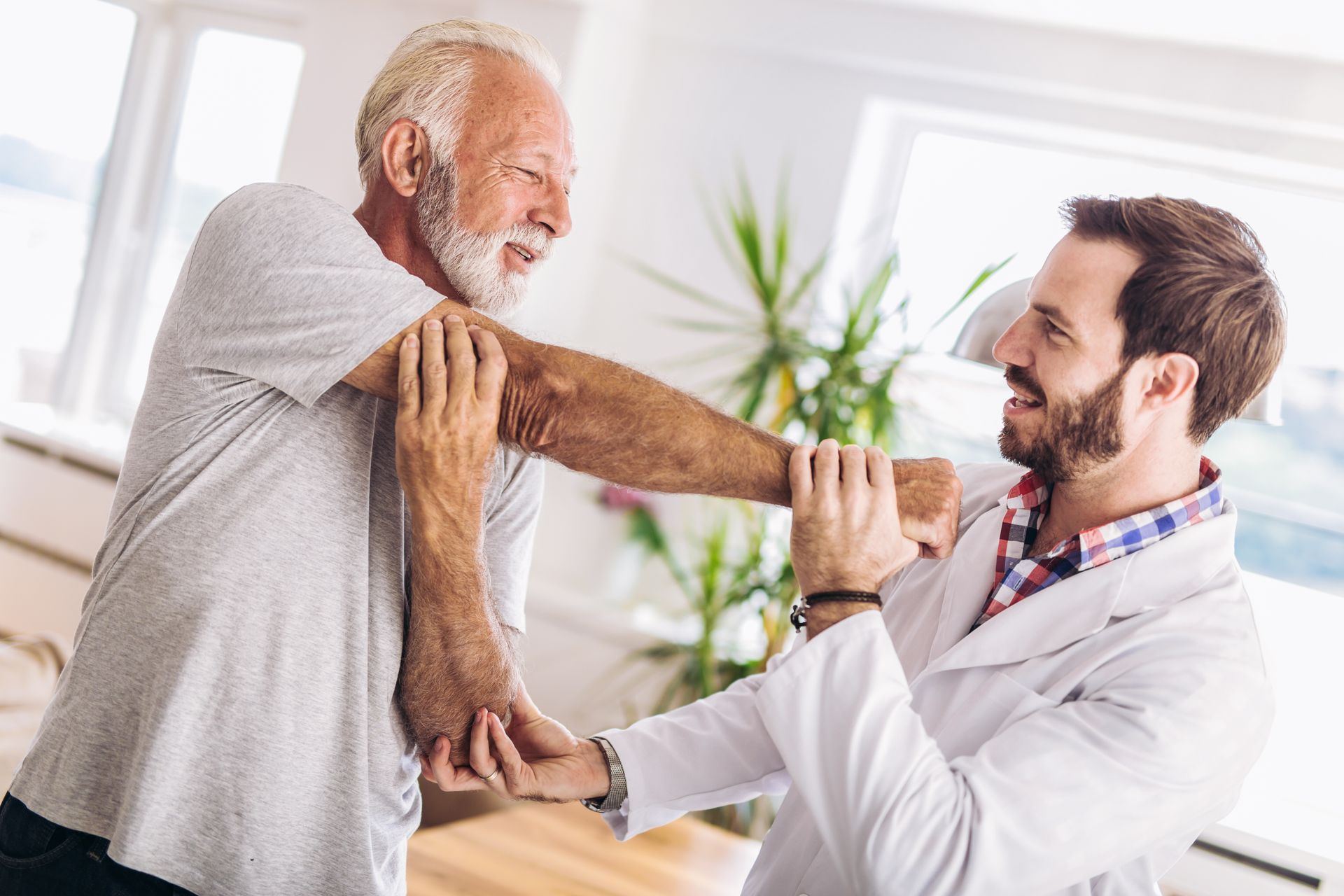 Doctor helping man stretch arm in bright clinic office