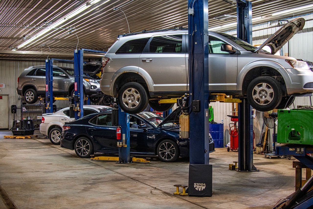 Cars on lifts in an auto repair shop. Silver minivan, blue car, and other vehicles are visible | Jackson, MI