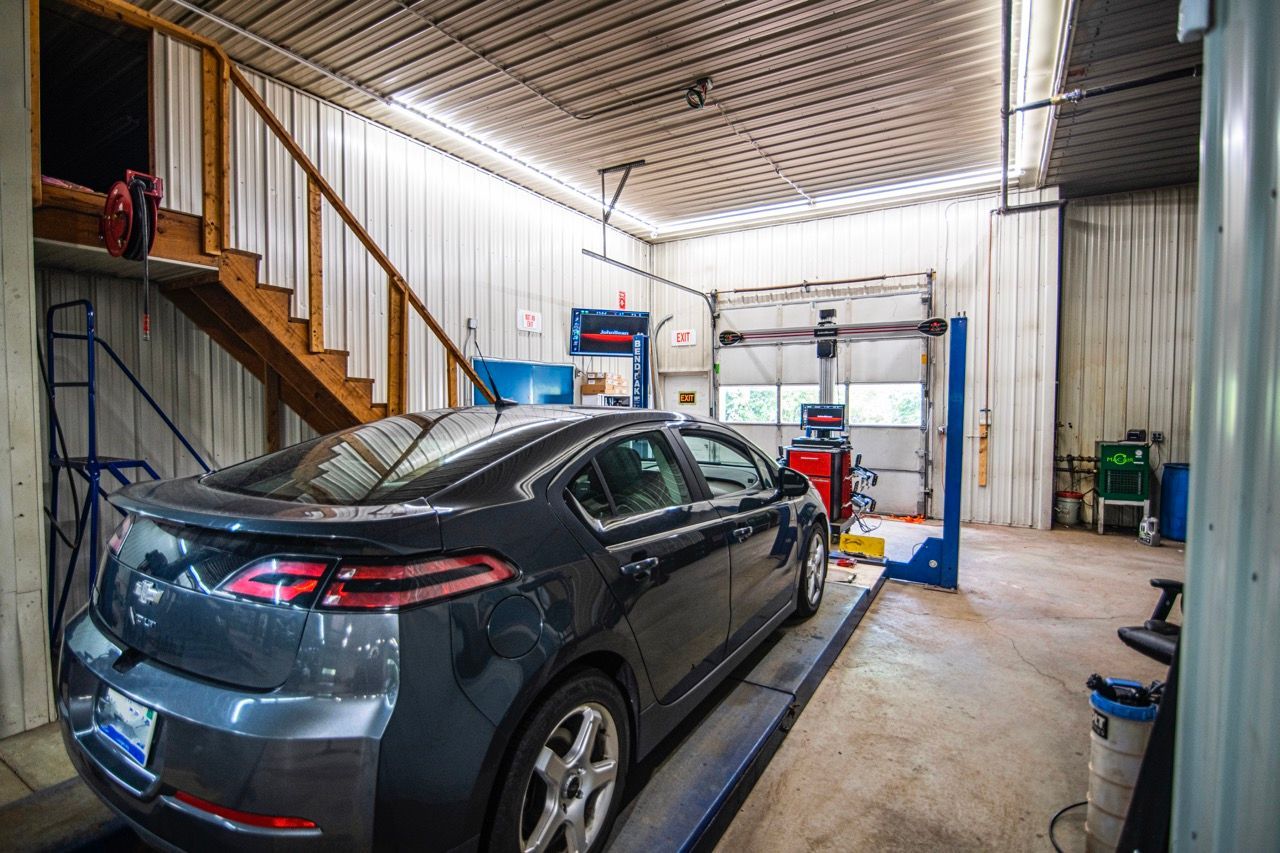 Grey car on a lift in a garage, stairs and equipment visible | Jackson, MI