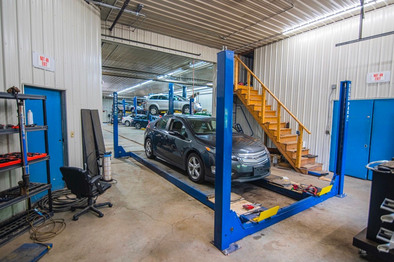 Car on a blue lift in a repair shop. Other cars are elevated, and there is a staircase | Jackson, MI
