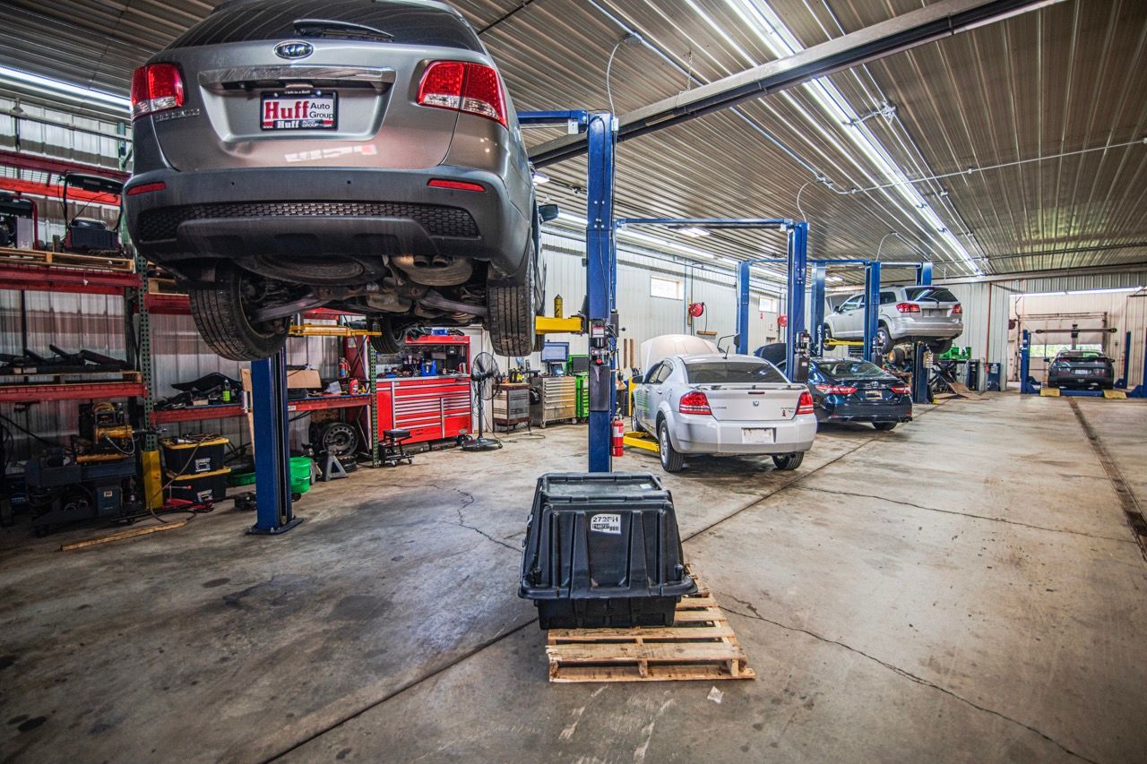 Cars on lifts in a repair shop. Interior shot with cars, tools, and a large black container on a pallet | Jackson, MI