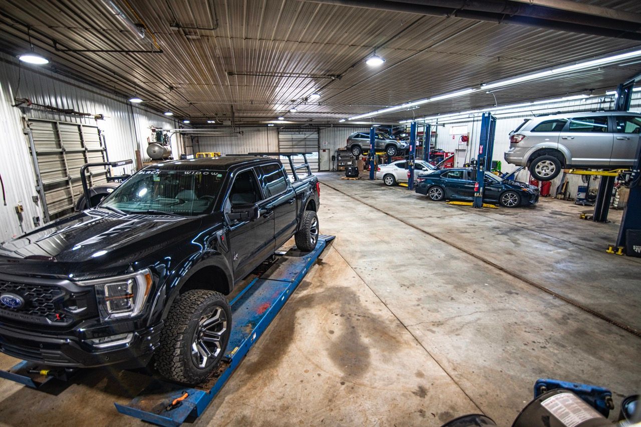 Black pickup truck on a lift in a busy auto repair shop with multiple vehicles being serviced | Jackson, MI