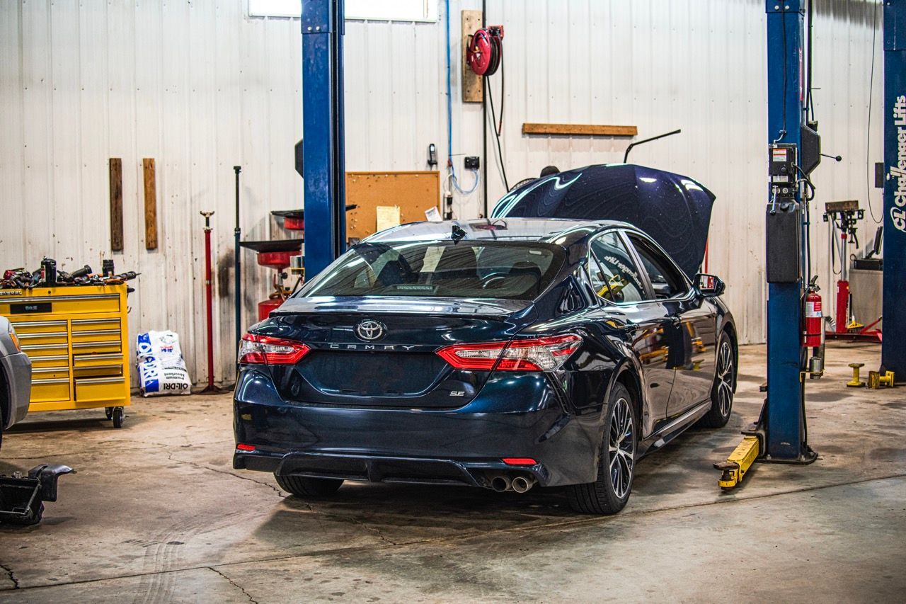 Blue car in a car repair shop with the hood open, being serviced on a lift | Jackson, MI