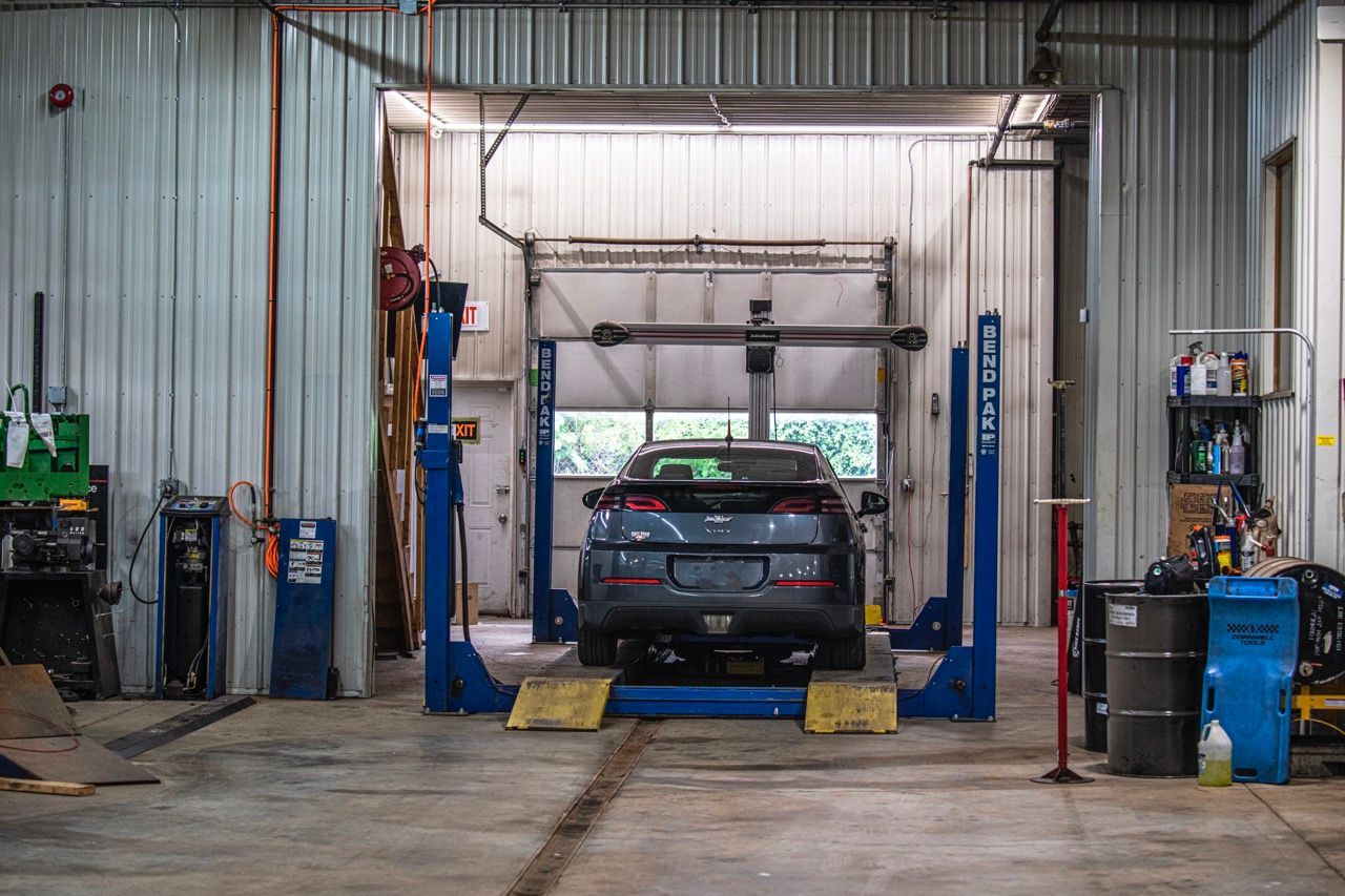 Car on a blue lift inside a garage, with tools and equipment visible | Jackson, MI