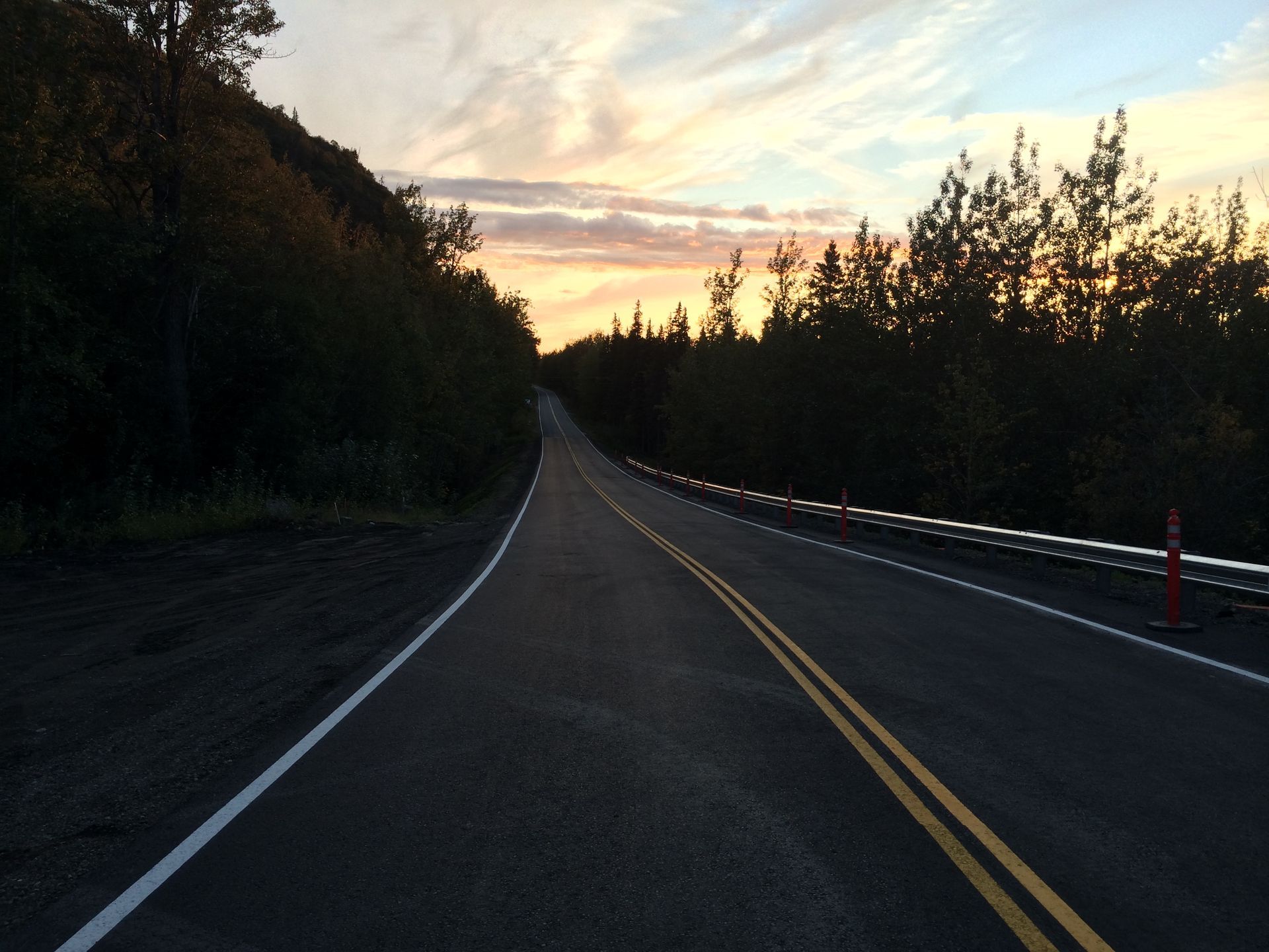 Empty road at sunset, with trees lining both sides and a painted centerline stretching into the distance