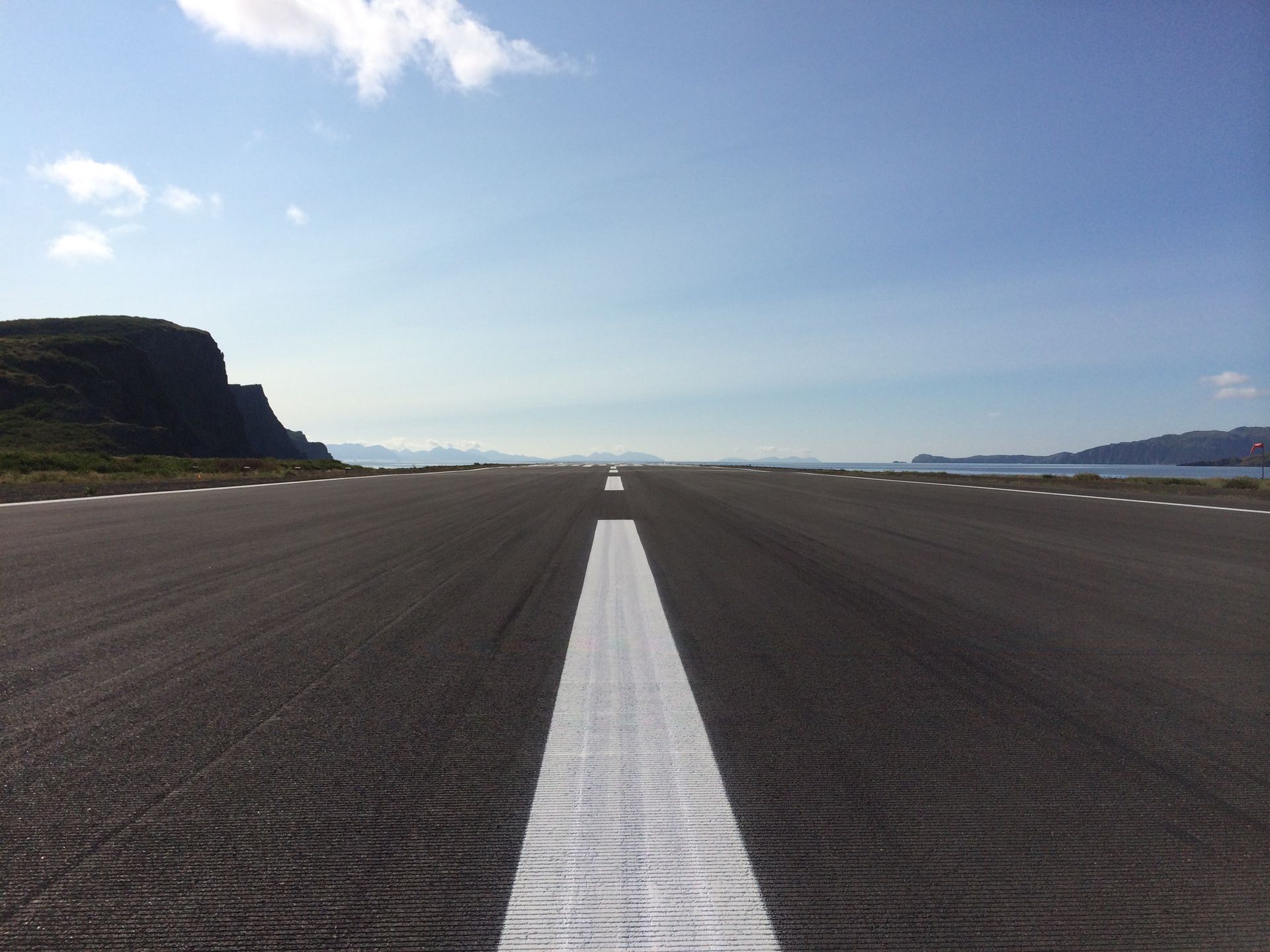 Empty runway stretching toward the horizon under a blue sky, with cliffs on the left and sea on the right