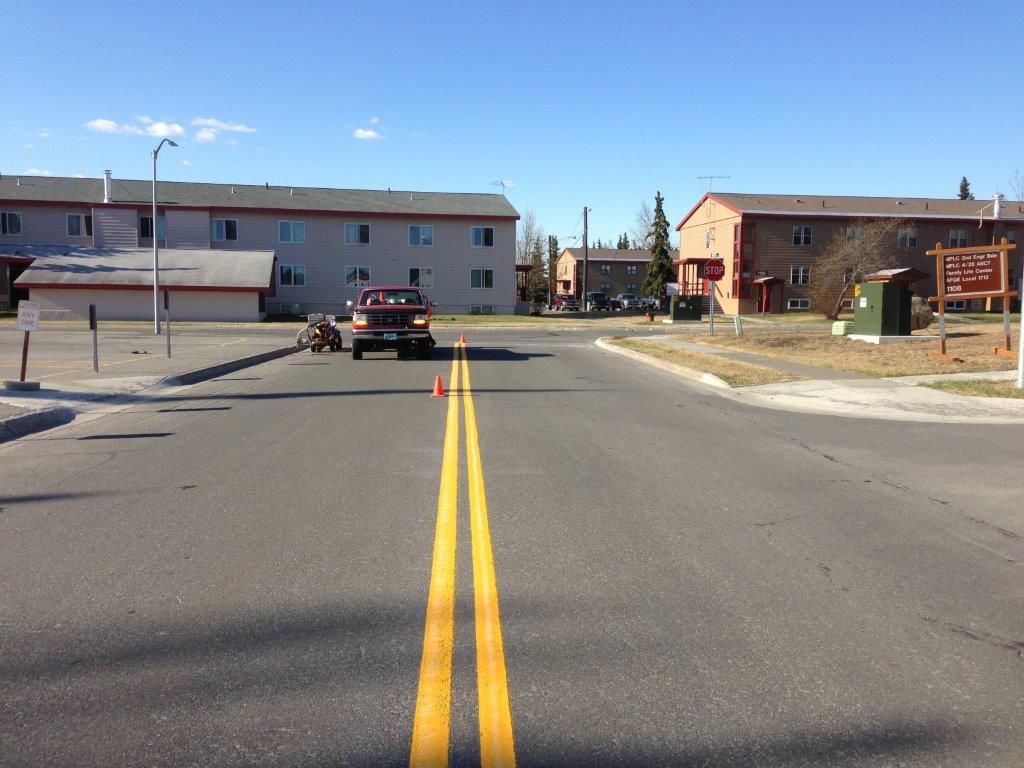 Street view of an intersection with double yellow lines, a car ahead, and apartment buildings on both sides