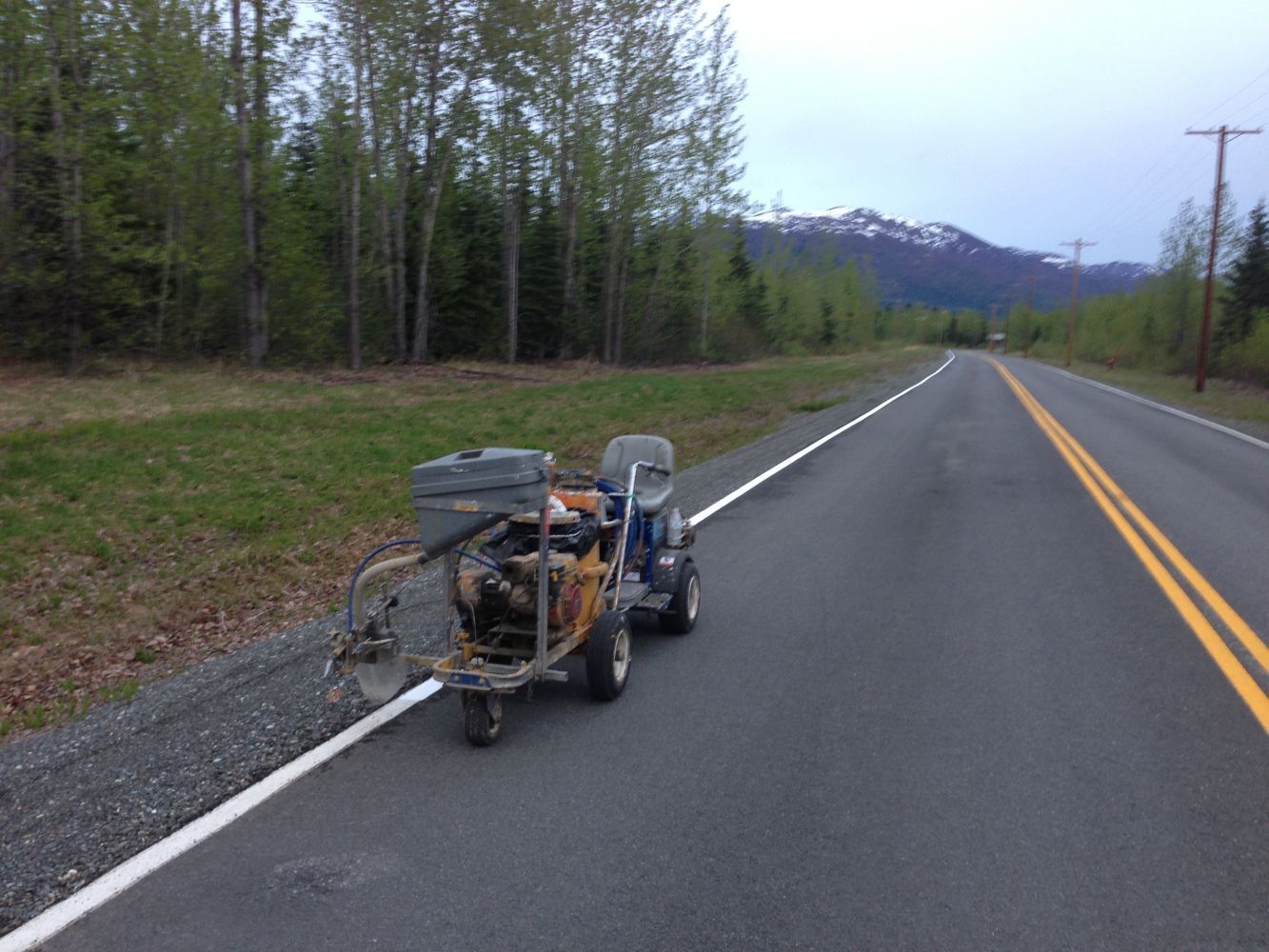 Loaded trailer parked on a rural road beside trees and mountains