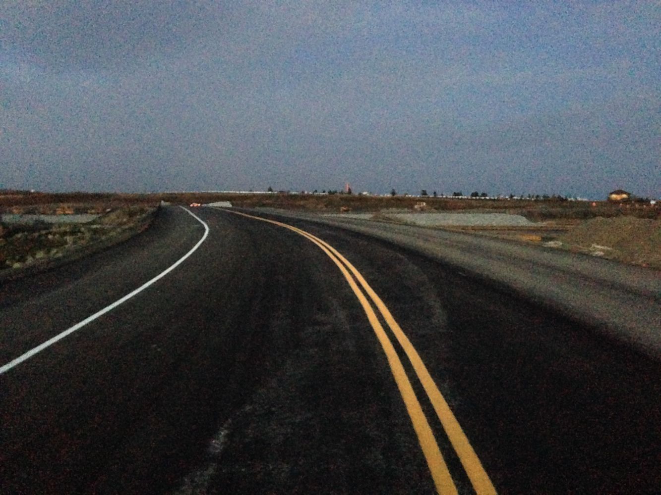 Empty winding road at dusk with double yellow lines through a flat landscape