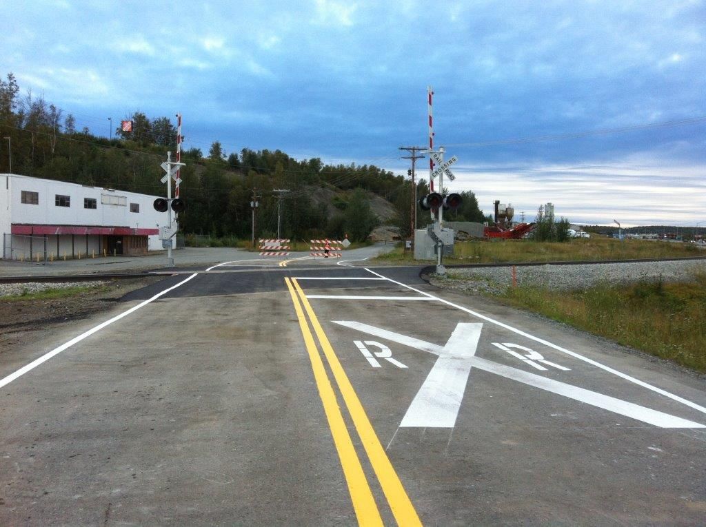 Rural road with double yellow lines, painted turn arrows, and a railroad crossing ahead under cloudy sky