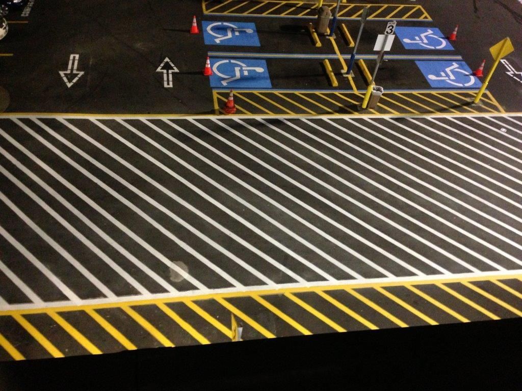 Diagonal white-striped accessible parking area with blue wheelchair spaces and yellow-black hazard markings