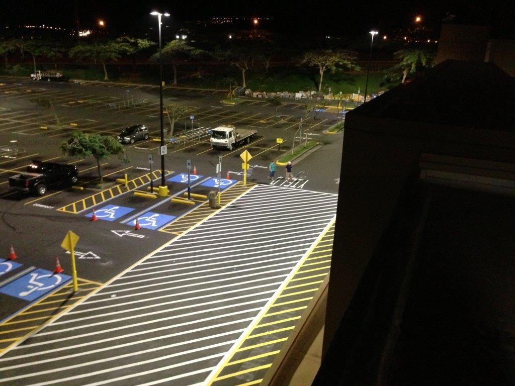 Nighttime parking lot with painted crosswalks, blue accessible spaces, and a parked van under streetlights