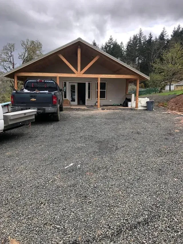 Gravel driveway leading to a small house with a parked SUV and trailer under an overcast sky