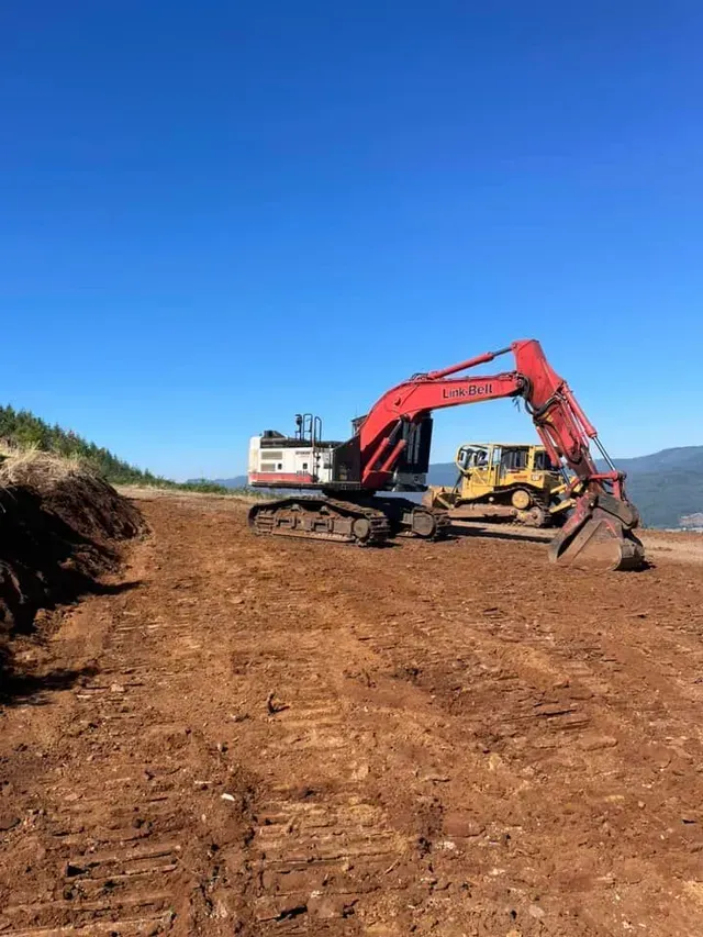 Red excavator and yellow bulldozer on a dirt construction site under a clear blue sky.