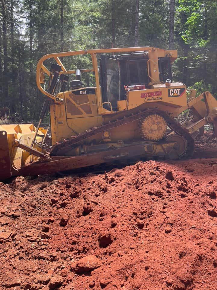 Yellow Caterpillar bulldozer on red dirt, working on a forested construction site.