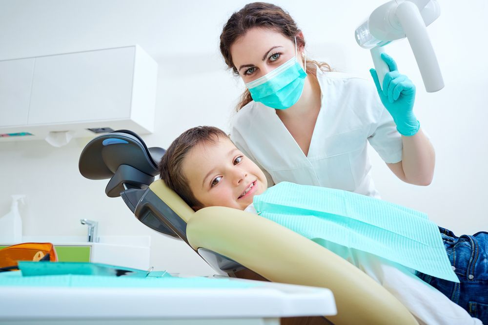 A Child in a Dental Chair Smiles at the Camera as a Dentist — Tamworth Orthocare In Narrabri, NSW