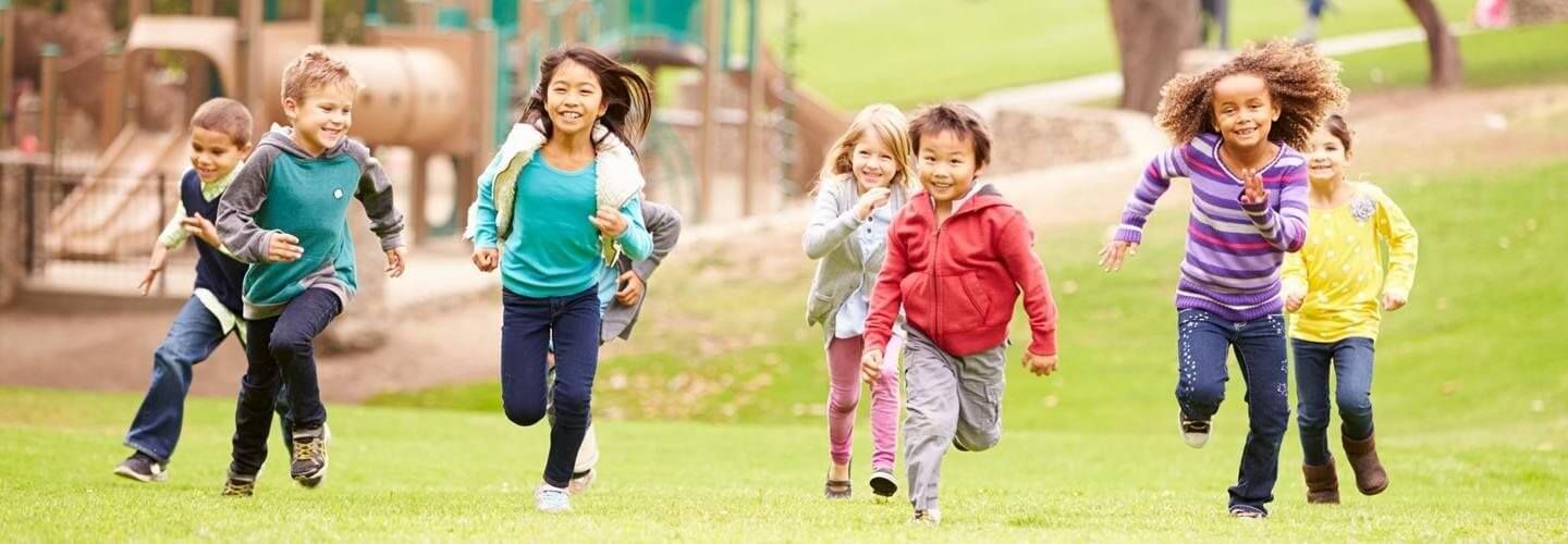 Children running and playing on a grassy field with colorful backpacks outdoors