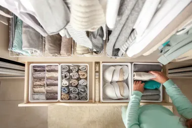 Top-down view of a clothing closet with folded garments and organized storage bins, a person sorting clothes.