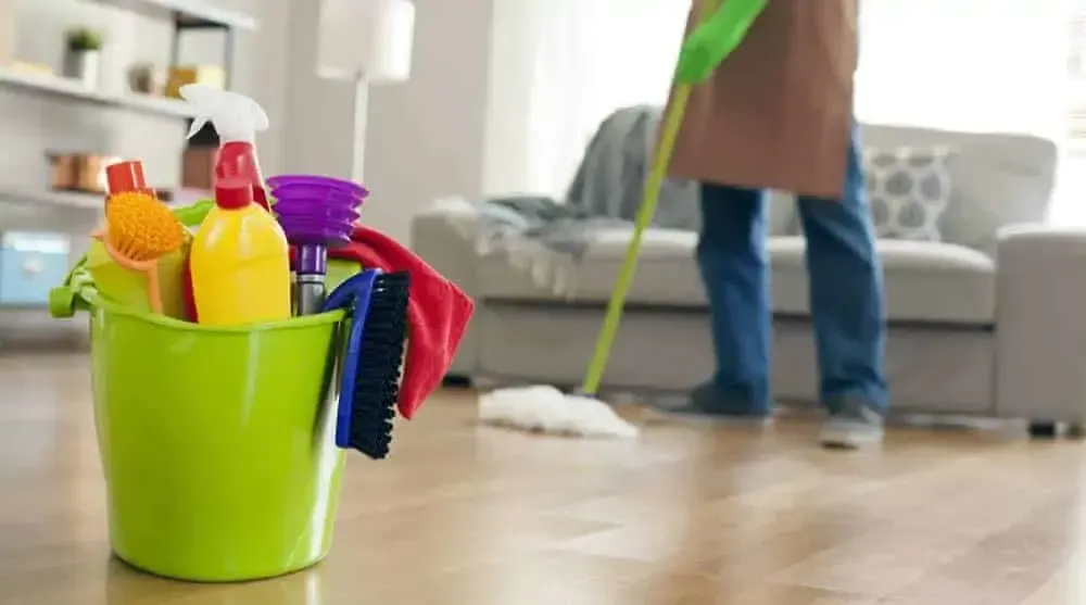 Person in orange gloves, clearing roots from a drain in a concrete floor, plumbing visible.