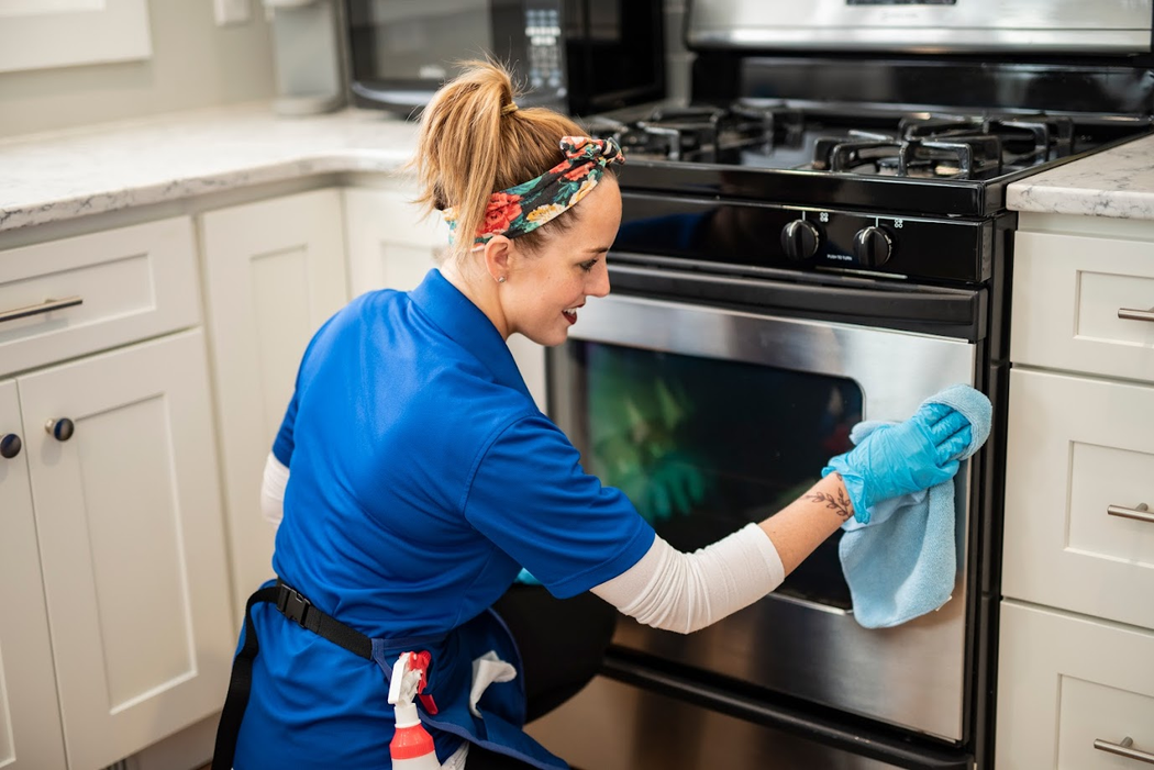 Woman cleaning an oven with a blue cloth in a bright kitchen