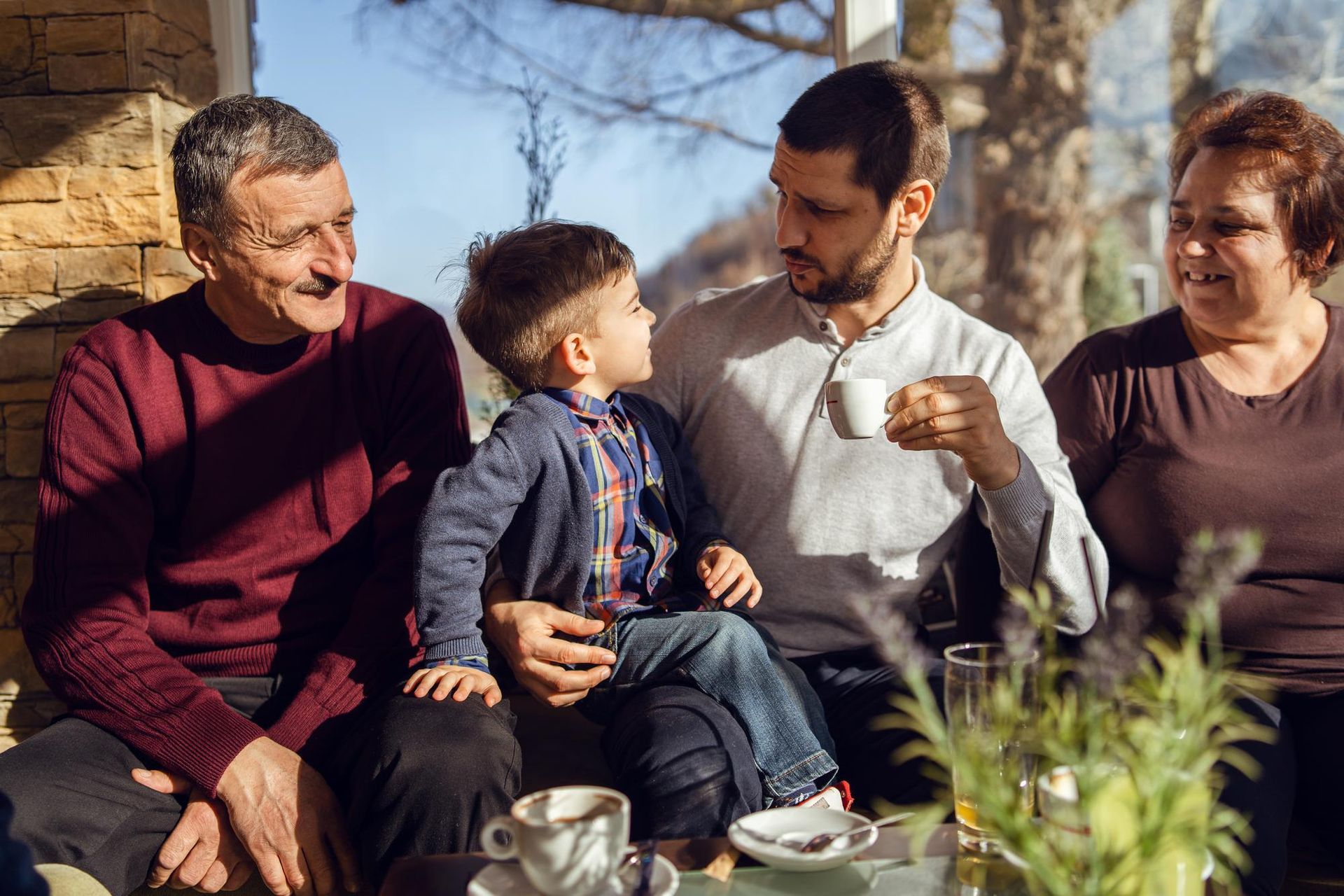 Four people sitting outdoors at a table, smiling and sharing drinks in a sunny garden.