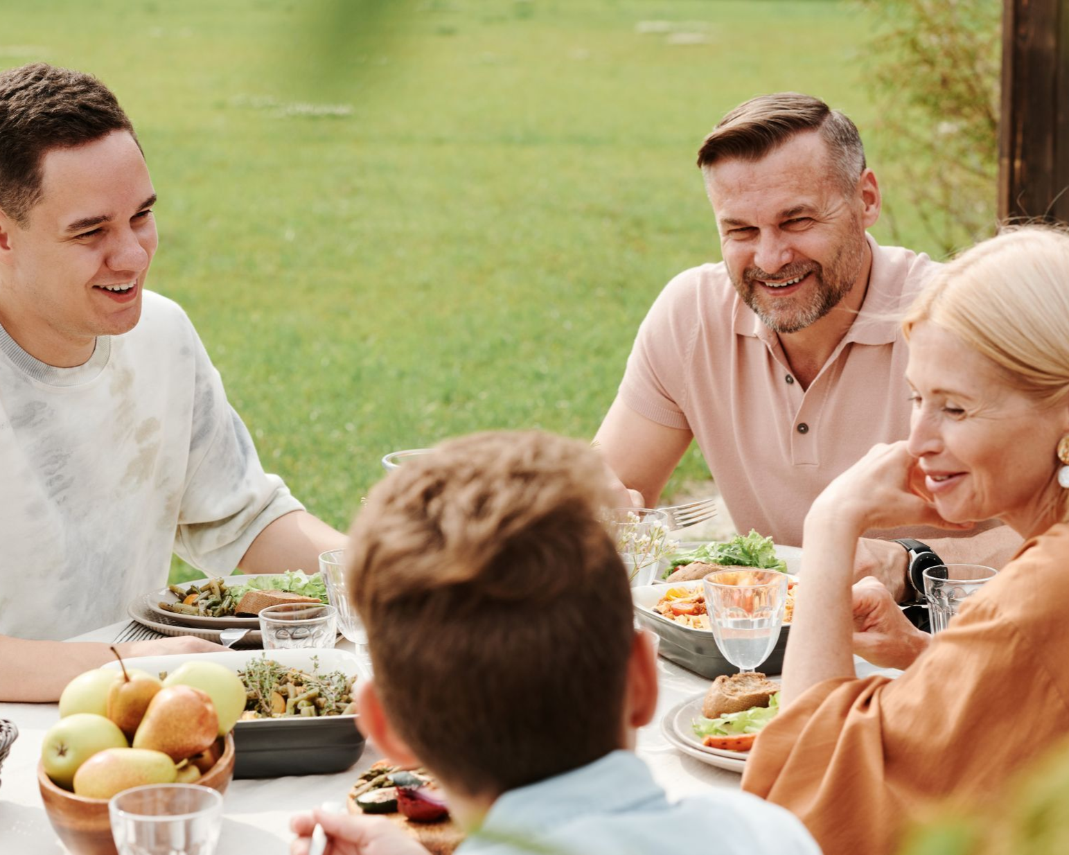 Friends sharing a meal outdoors at a picnic table, smiling in a sunny garden.