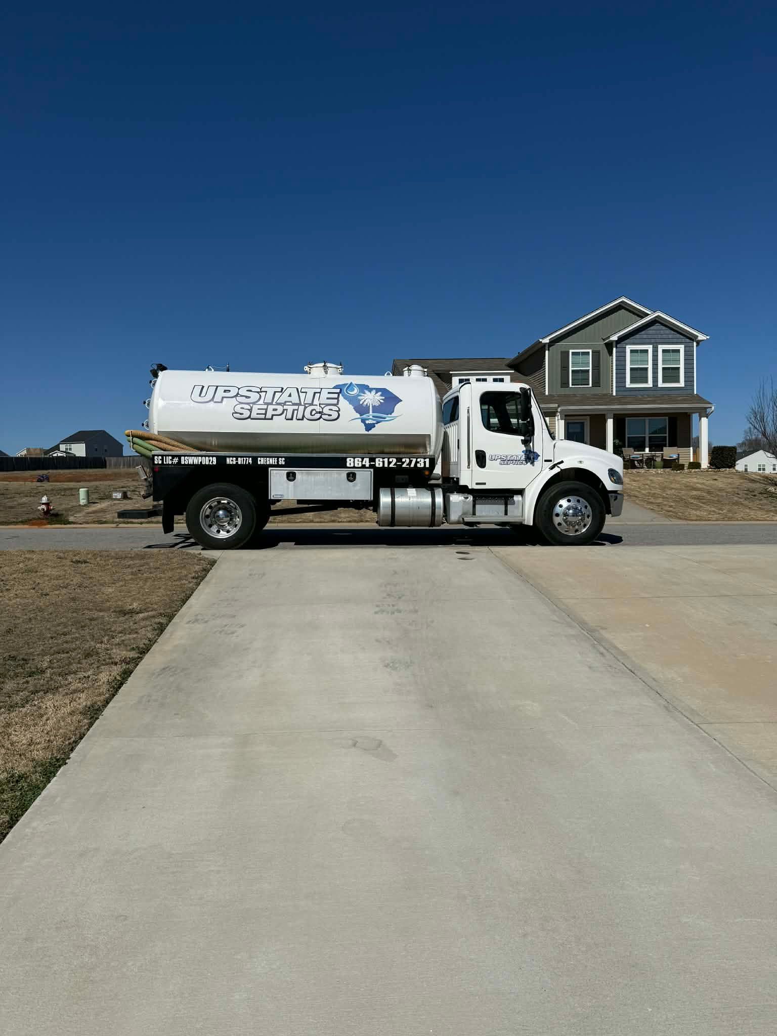 A white water truck with a South Carolina graphic sits parked on a concrete driveway in front of a house.