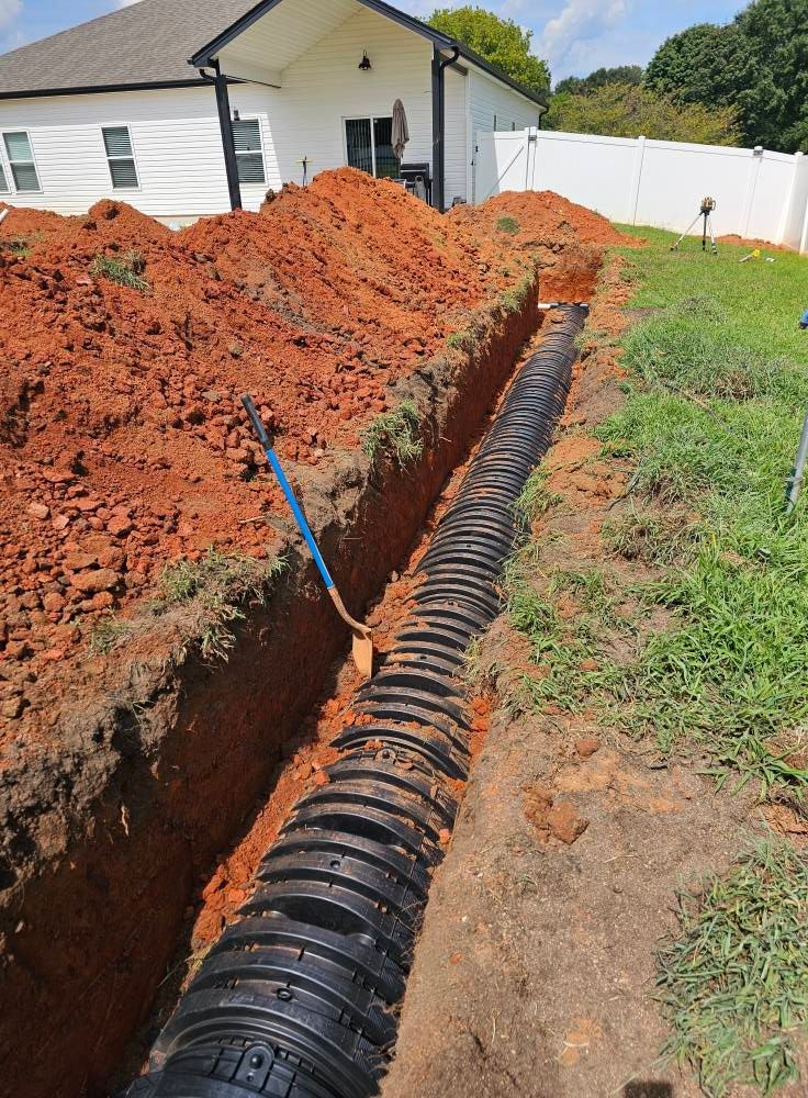 A black plastic drainage chamber system installed in a deep trench next to a house under construction.