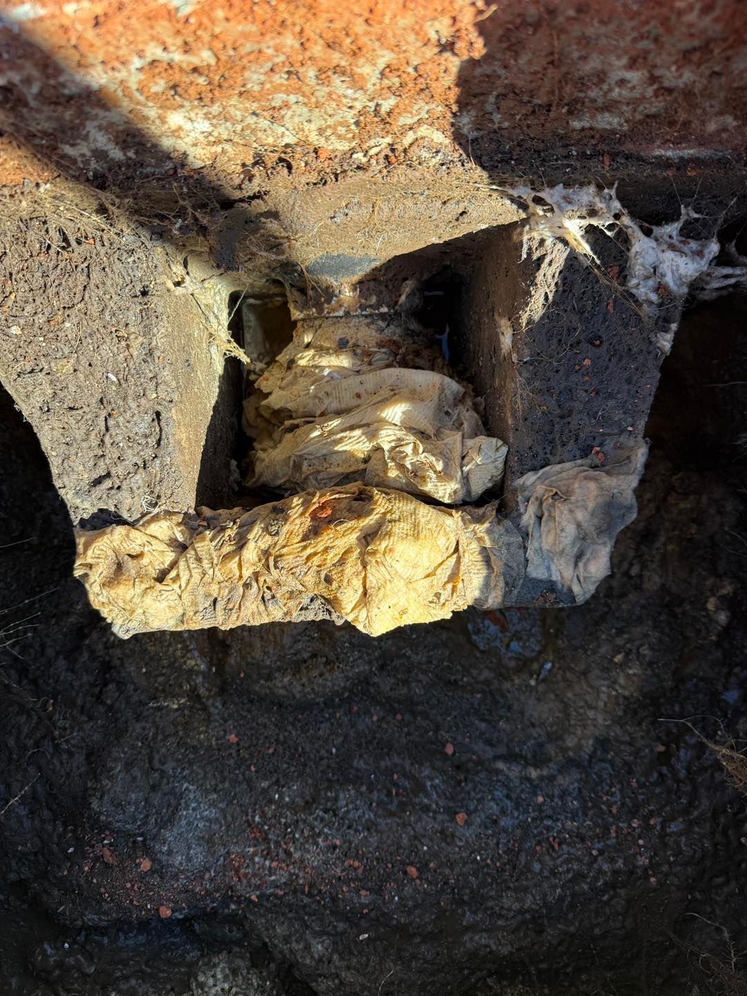 A close-up view of a damaged masonry wall corner with exposed, crumbling aggregate and hardened yellow foam filler.