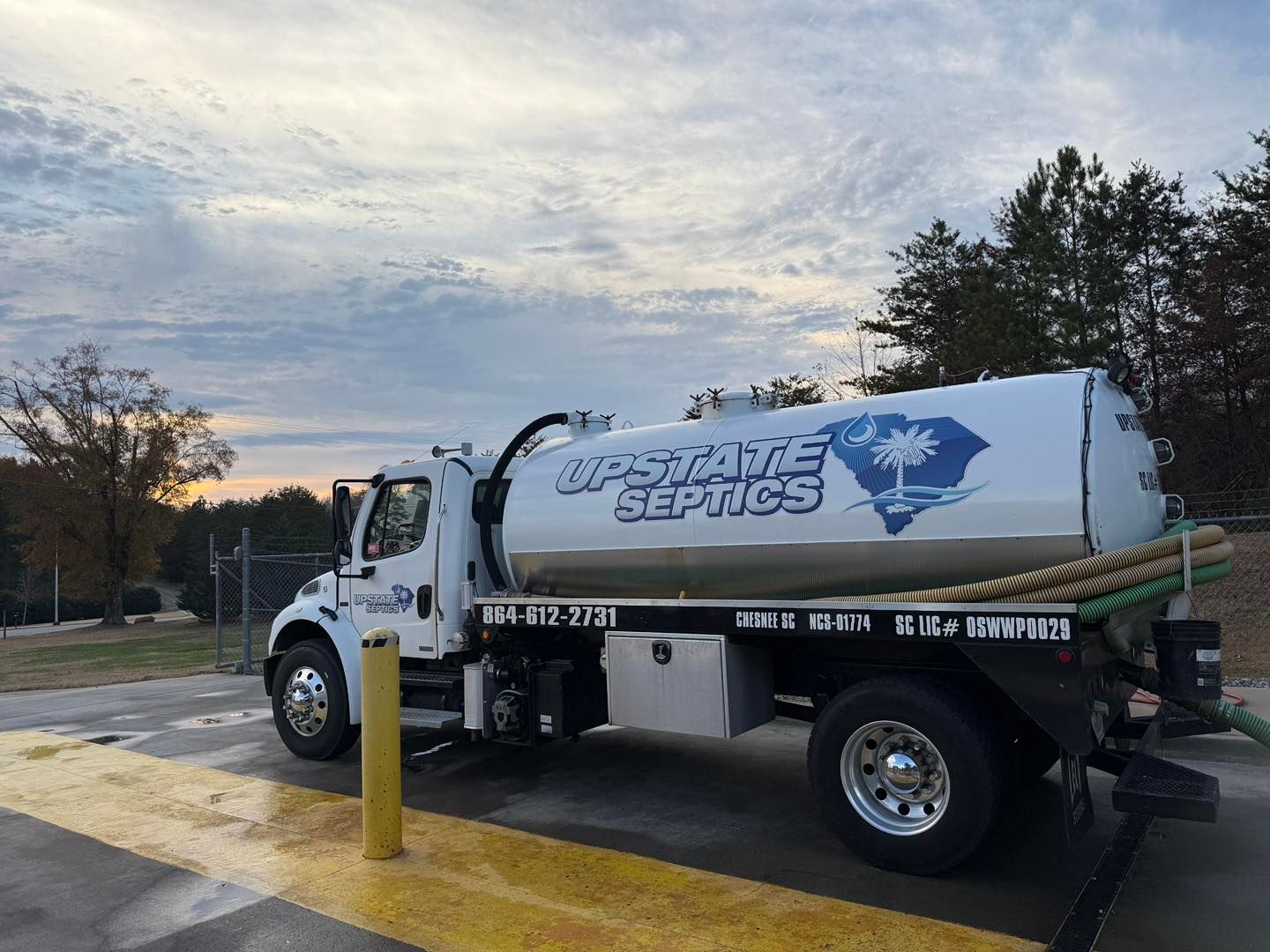 A white Upstate Septics truck parked on a paved lot at sunset with trees in the background.